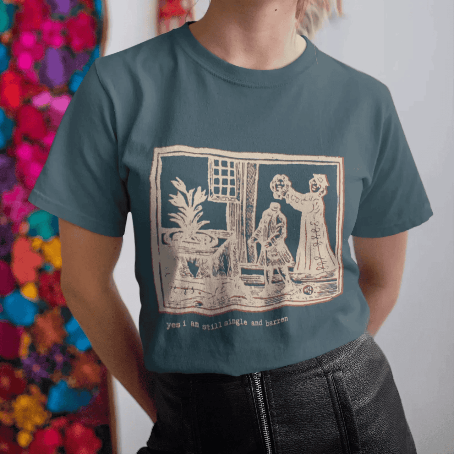Woman wearing a petrol blue classic t-shirt with a graphic design and text, saying, yes, I am still single and barren.