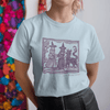 May my dog also attend? - woman in pale blue staple t-shirt with medieval woodcut style illustration of witches with a demon-