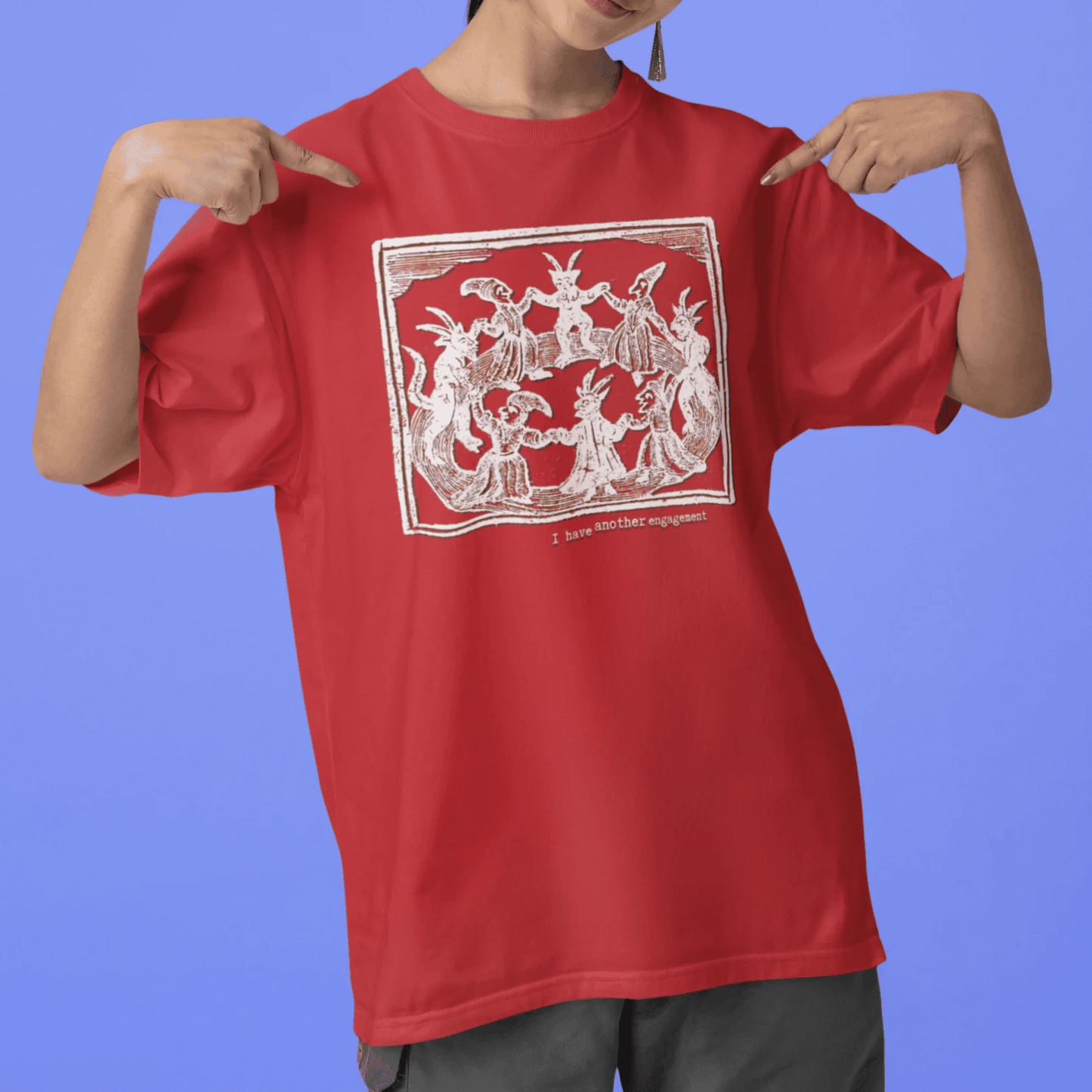 I have another engagement - woman wearing a red staple t-shirt with medieval woodcut illustration showing witches dancing in 
