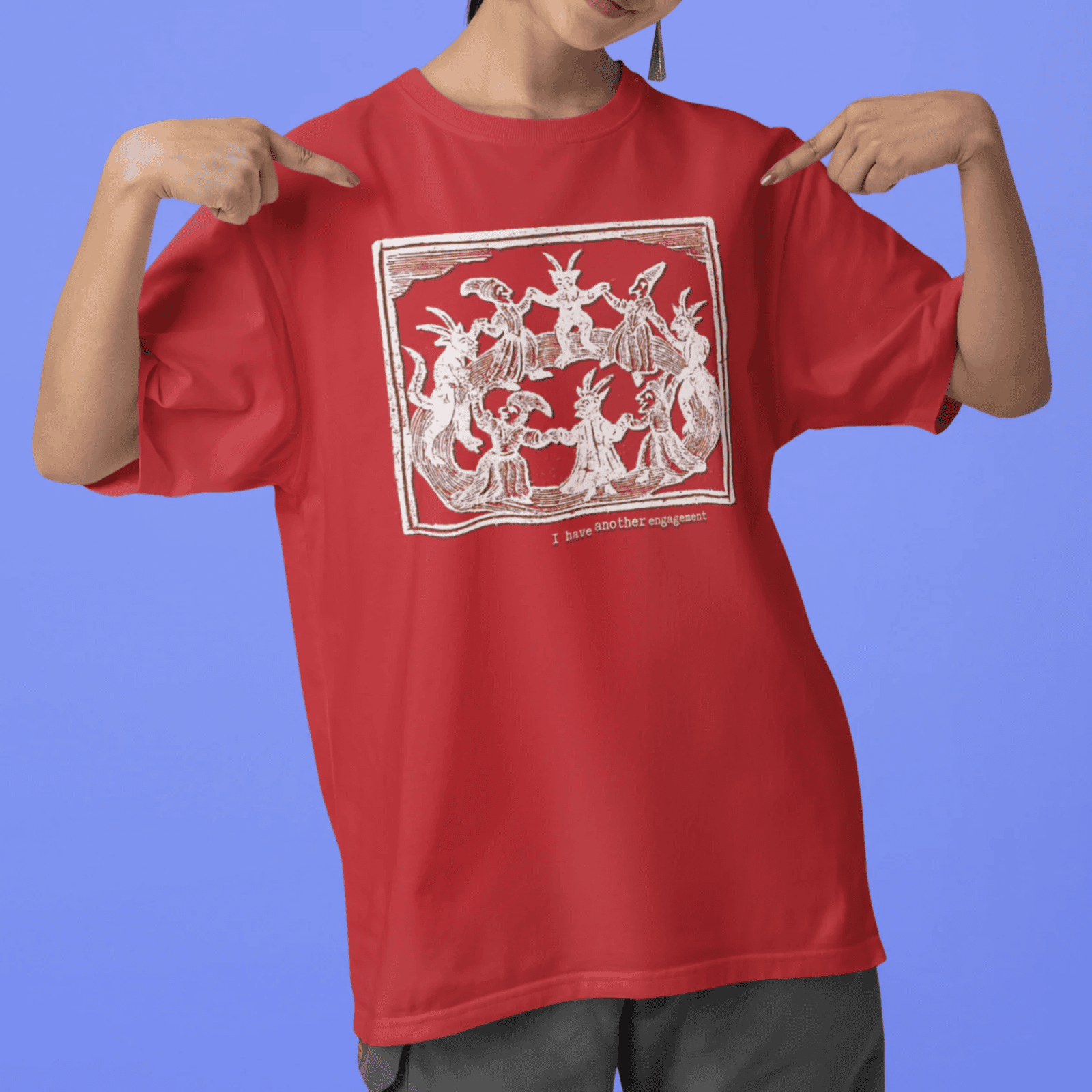 I have another engagement - woman wearing a red staple t-shirt with medieval woodcut illustration showing witches dancing in 