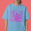Woman wearing carolina blue staple t-shirt with hot pink medieval woodcut style design of witches with a demon-dog saying "ma