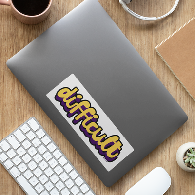 Laptop with a 'difficult' sticker on a wooden desk with keyboard, mouse, and coffee cup.